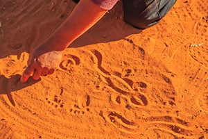 aboriginal woman hands creating shapes with red sand on the ground in aboriginal art style Northern Territory